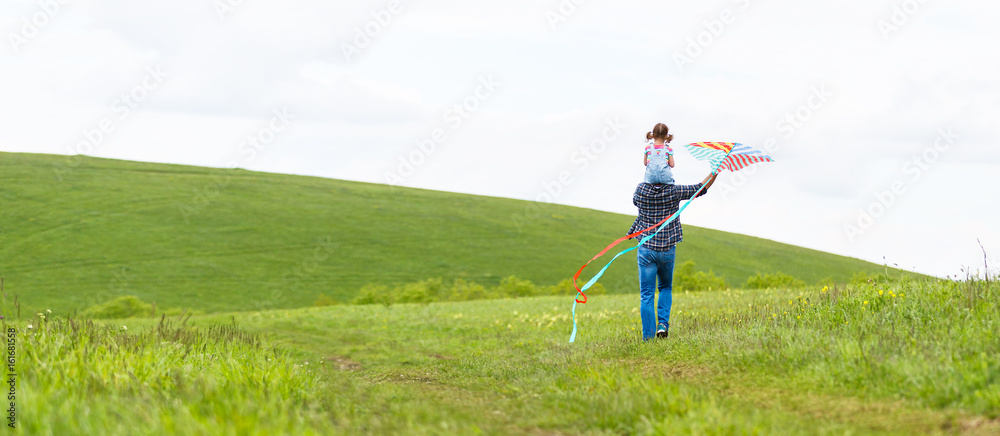 幸福的家庭父亲和小女儿在草地上放风筝跑步。