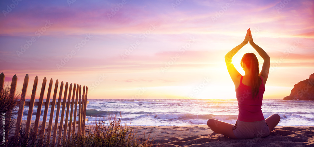 日落时在海滩上做瑜伽健身的女人