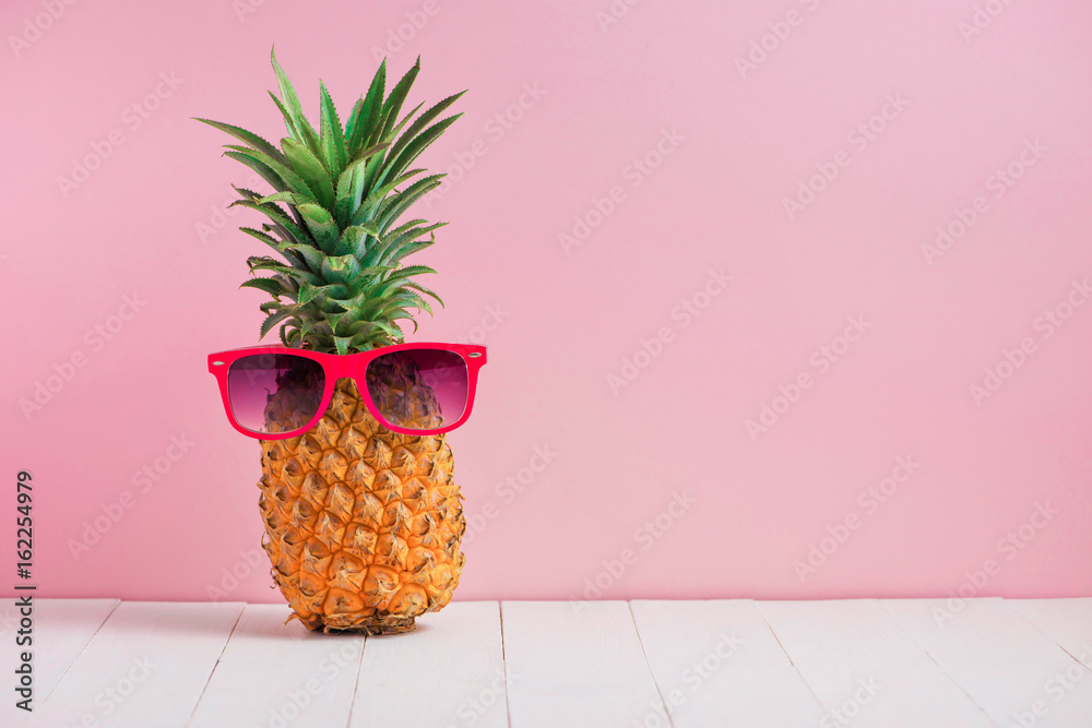 粉色背景下，桌子上戴着太阳镜的有趣菠萝