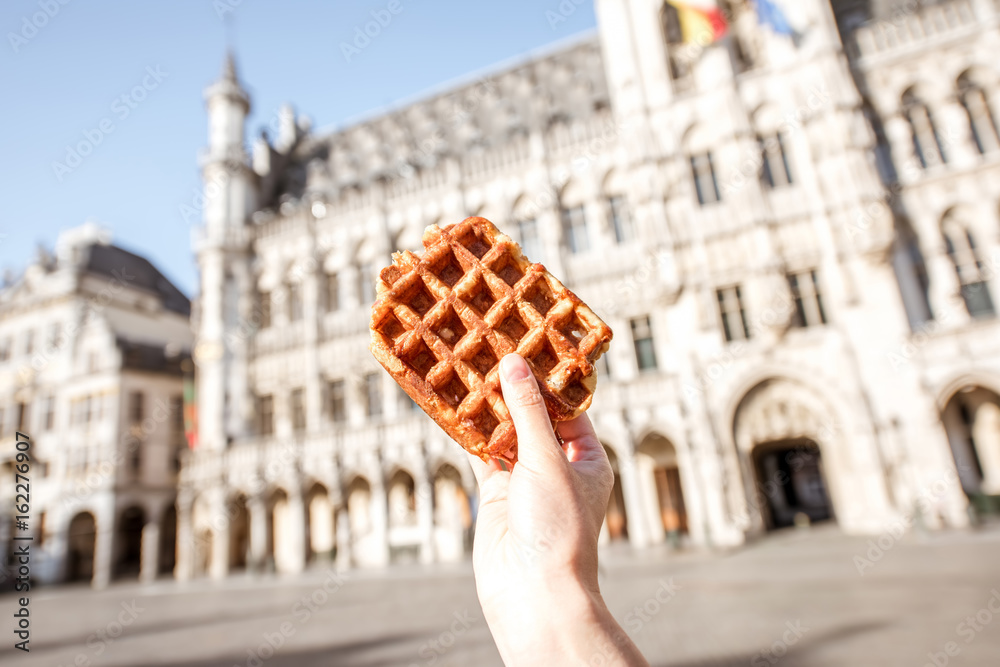 Holding a traditional belgian waffle on the central square background with city hall in Brussels. Be