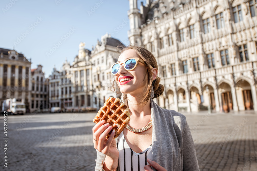 布鲁塞尔市中心，一名年轻女子拿着华夫饼行走，华夫饼是一种传统的比利时糕点