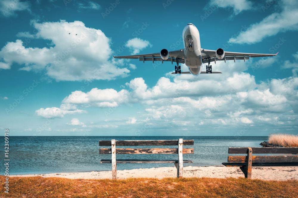 Beautiful airplane and wooden bench at the sea. Landscape with white passenger airplane is flying in