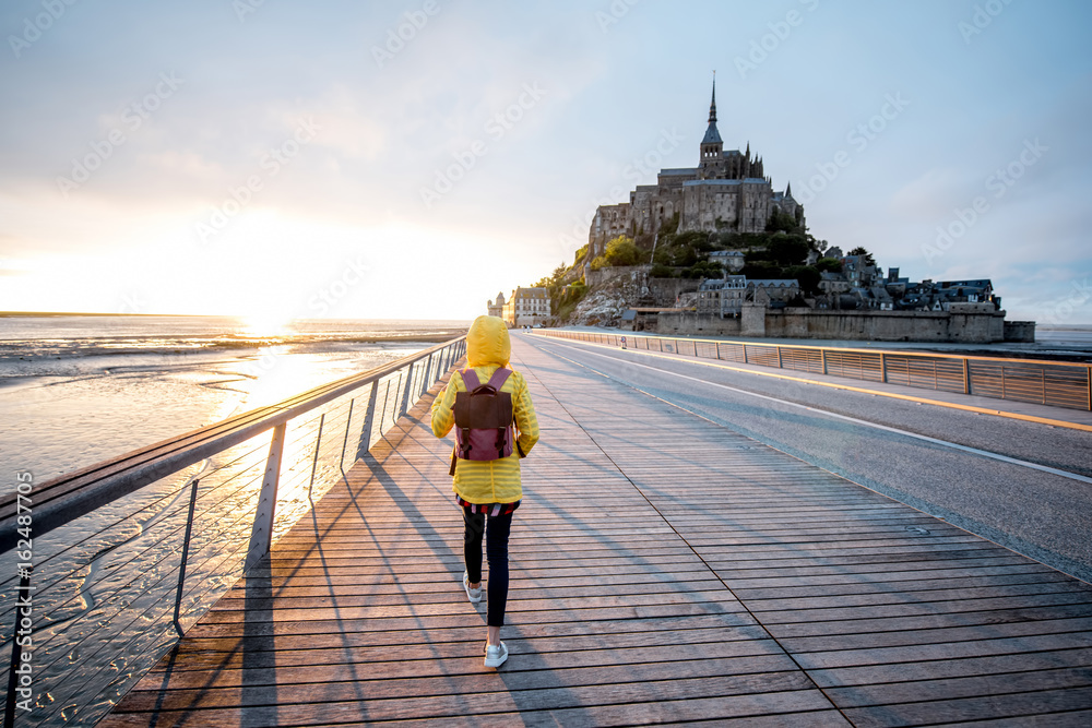 穿着黄色雨衣的年轻女旅行者在前往法国著名圣米歇尔岛的路上
