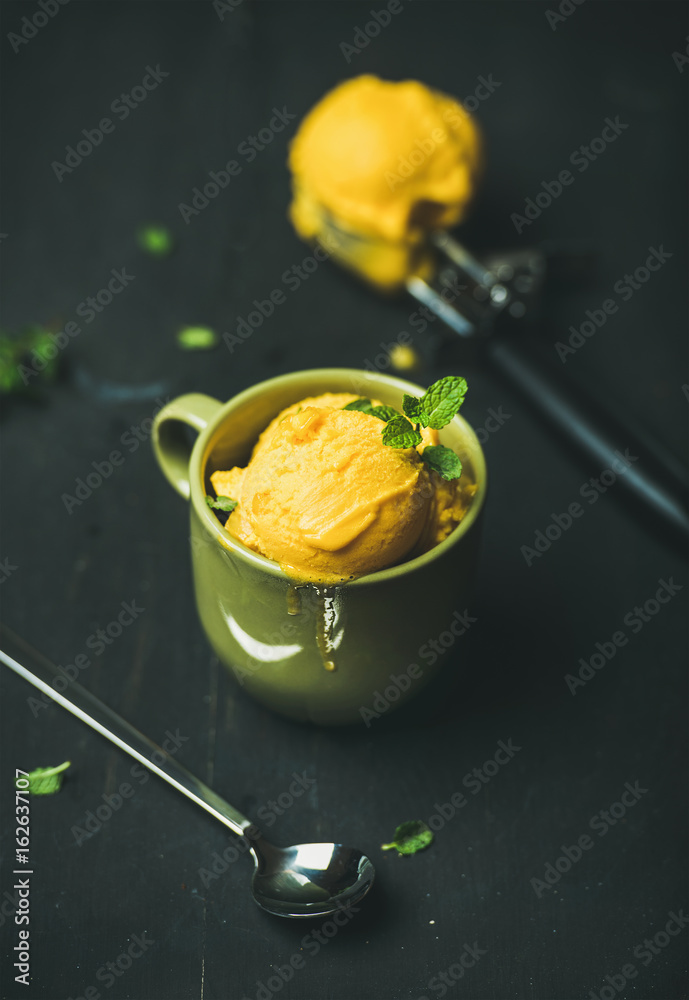 清爽的夏季甜点。芒果冰糕冰淇淋勺，绿色杯子里放着新鲜的薄荷叶。