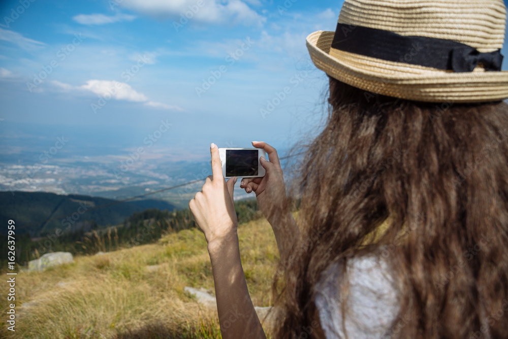 Girl with smartphone on the slope of the mountain of Vitosha and the blue sky. View of the city of S