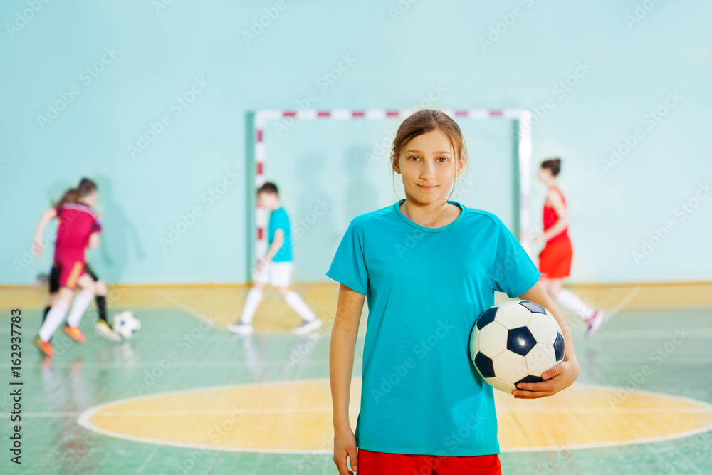 女孩拿着足球站在学校体育馆里