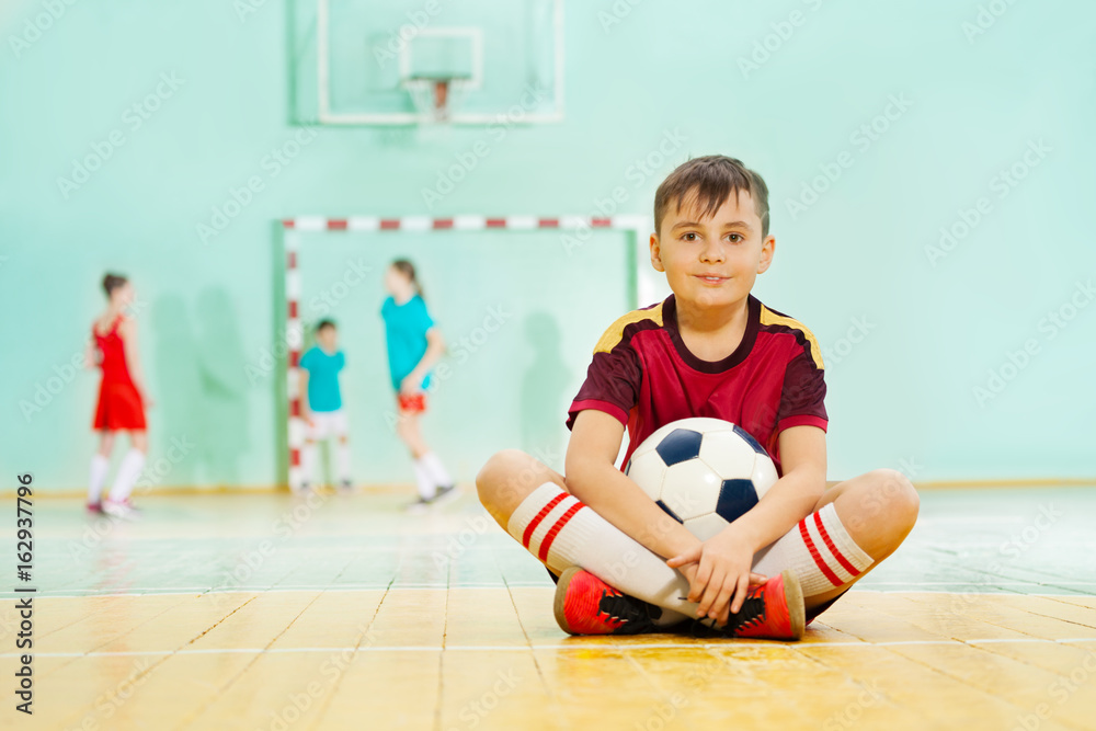 快乐男孩拿着足球坐在地板上