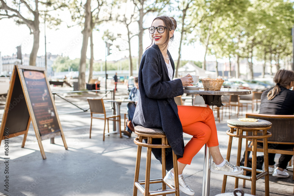 一位年轻女士坐在里昂的法国咖啡馆户外吃早餐，配咖啡和羊角面包