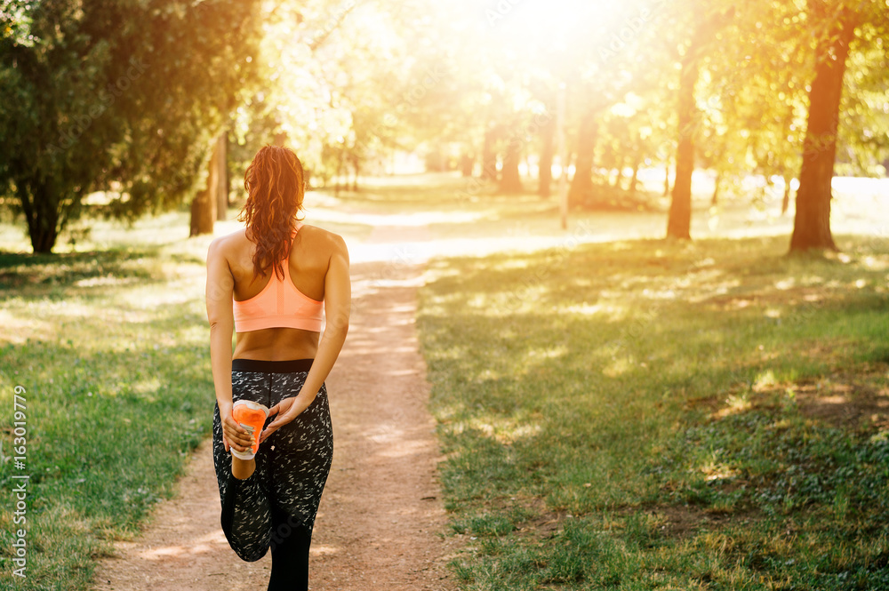 年轻的女跑步者在城市公园里伸展腿，后视图。