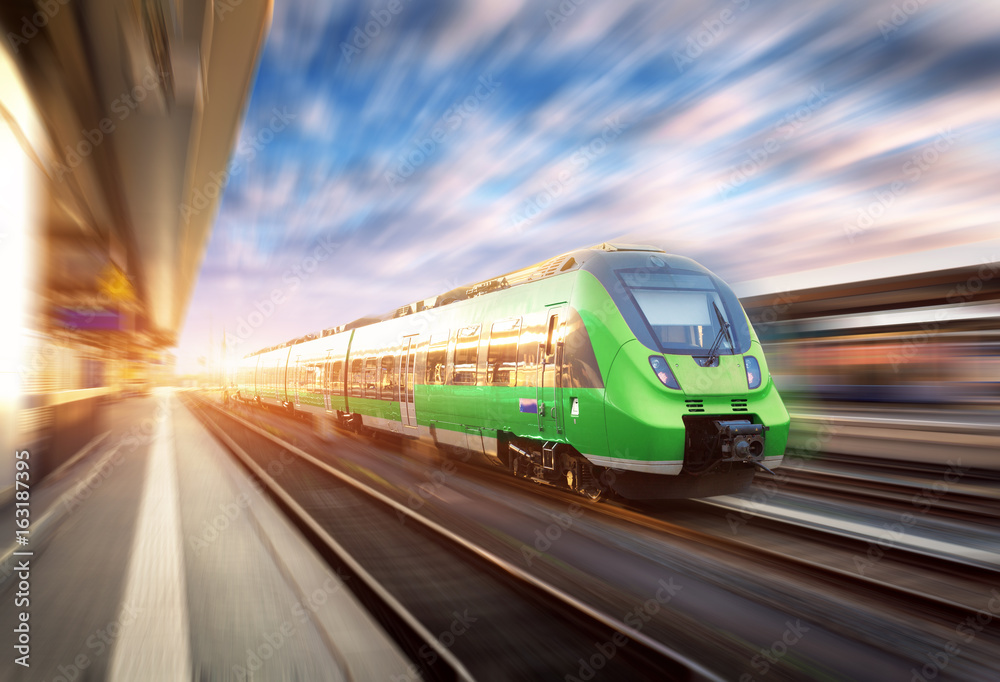 High speed train in motion at the railway station at sunset in Europe. Beautiful green modern train 