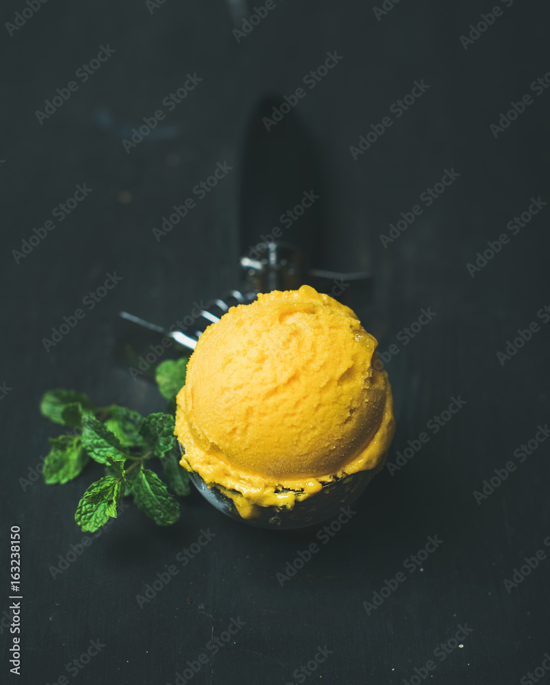 芒果冰糕冰淇淋勺装冰淇淋勺，黑色木质背景上有新鲜薄荷。Clea