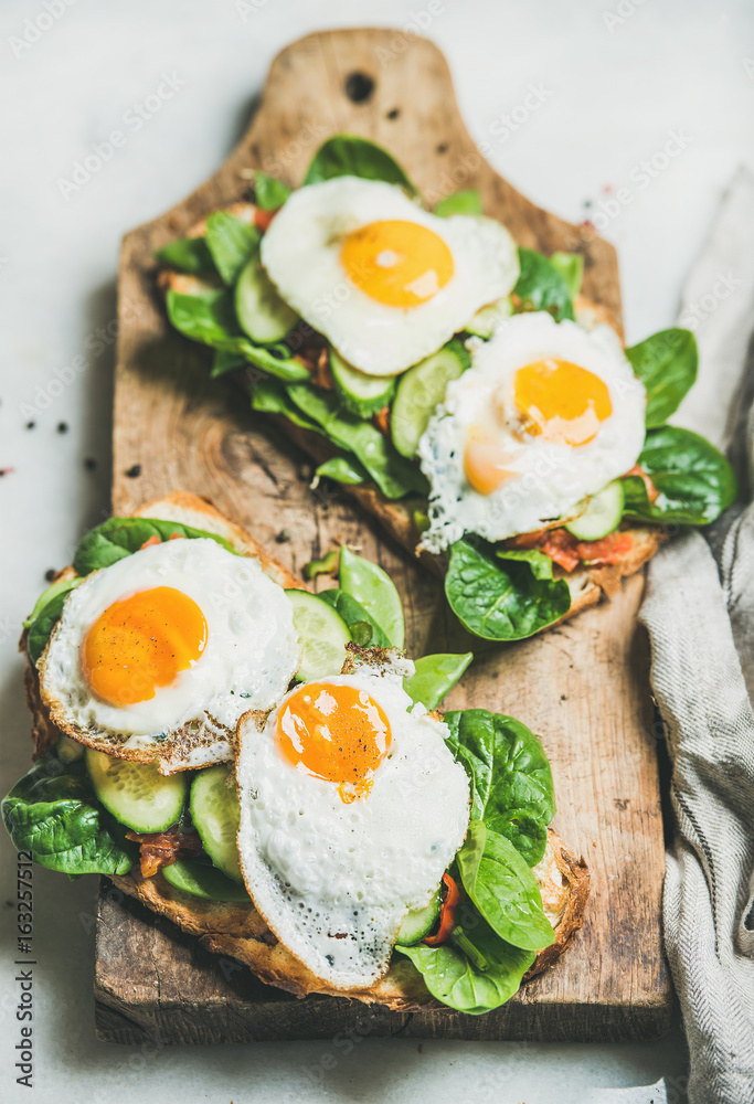 健康的早餐三明治。在木板上烤面包，配煎蛋和新鲜蔬菜