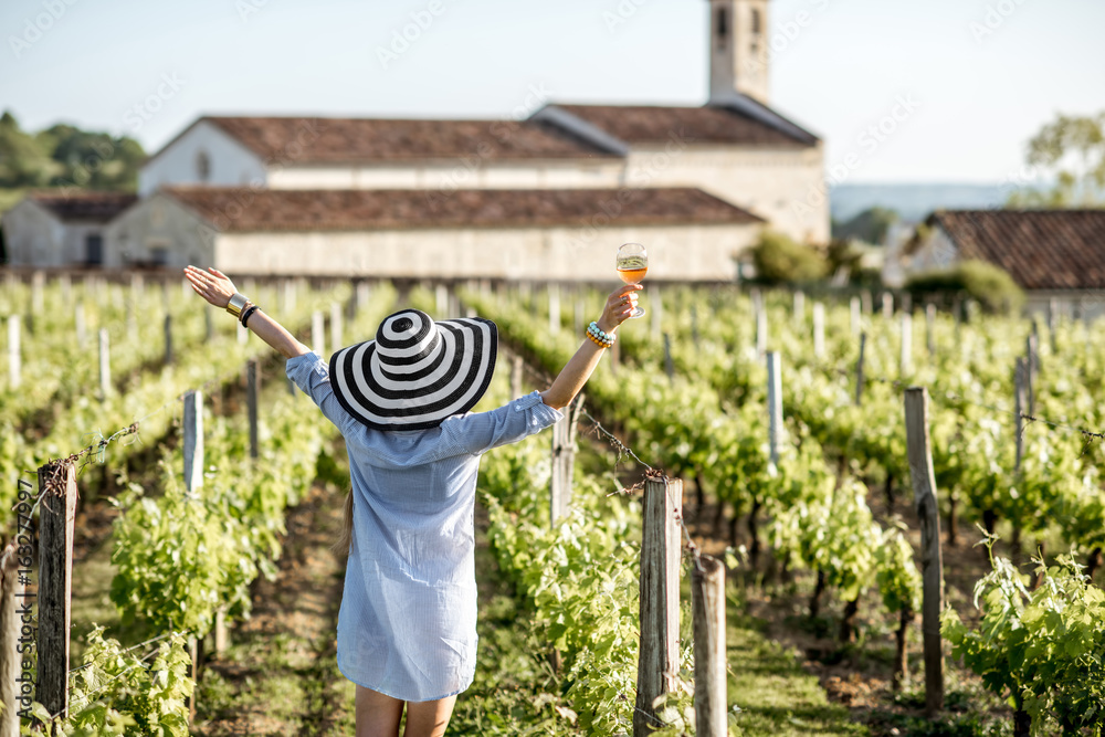 年，一位年轻女子拿着一杯葡萄酒在波尔多地区的葡萄园欣赏美丽的日落。