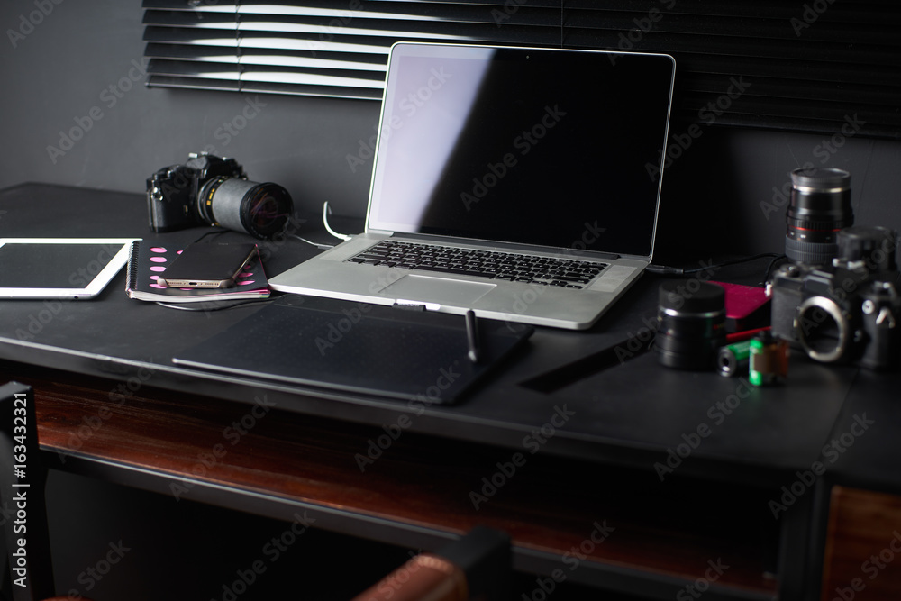 摄影师或设计师黑色桌子上的工作空间，带笔记本电脑、复古相机、时尚家居设计师
