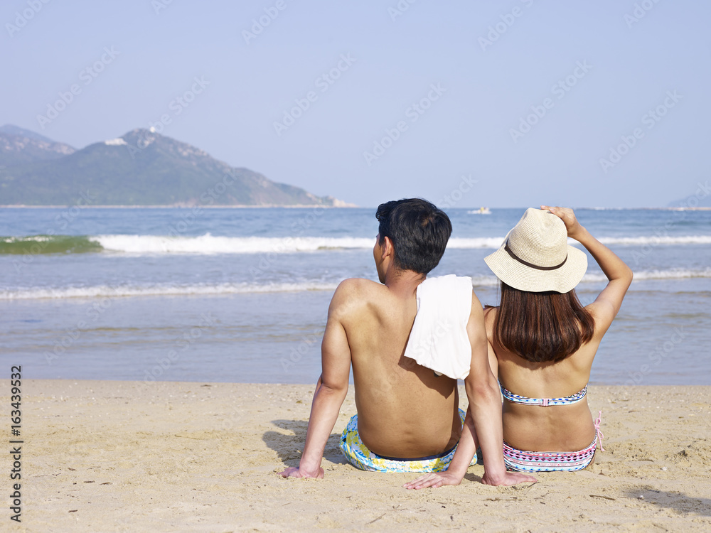 young asian lovers sitting on beach