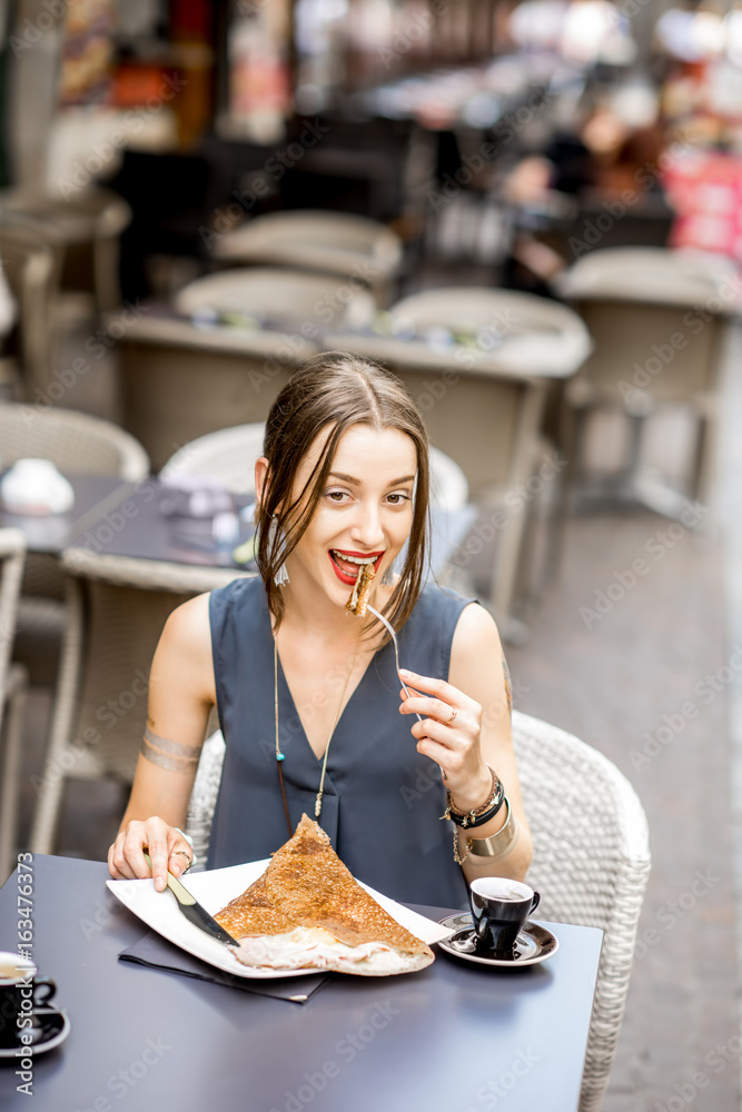 一位年轻女子坐在户外餐厅吃早餐，吃的是法国煎饼galette