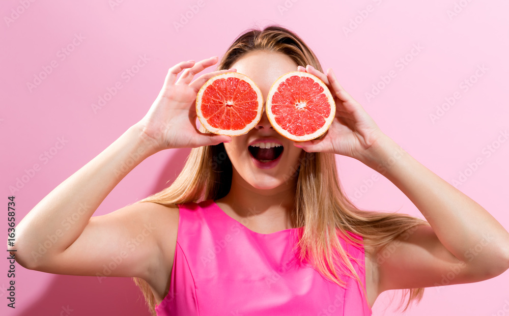 幸福的年轻女人在粉色背景上拿着两半葡萄柚