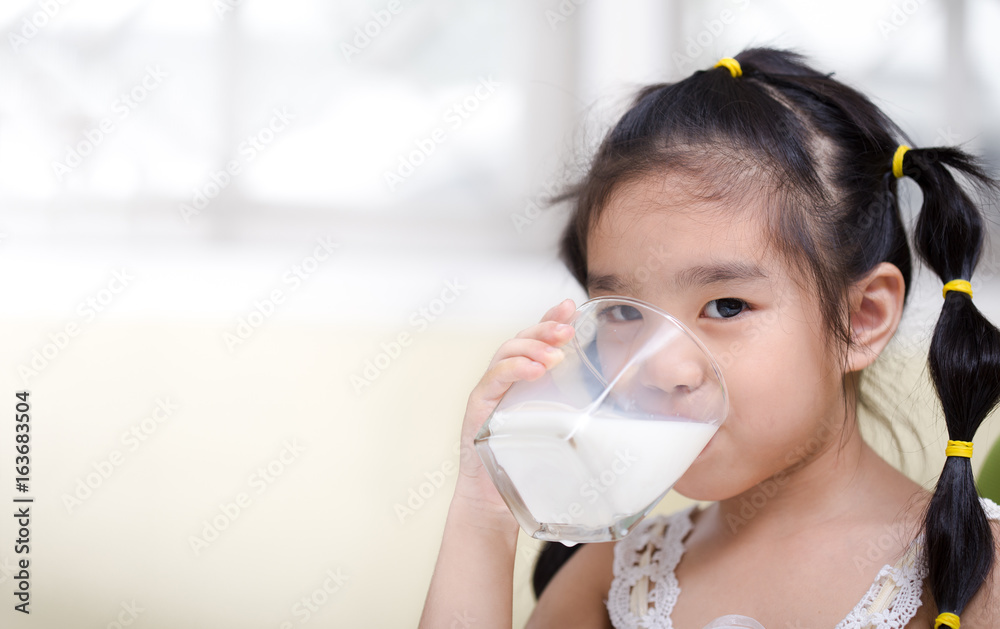 亚洲女孩在客厅背景上喝了一杯牛奶