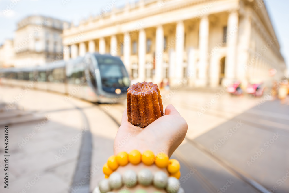 Holding a traditional Bordeaux sweet cake called Canele outdoors on the street near the Grand theatr
