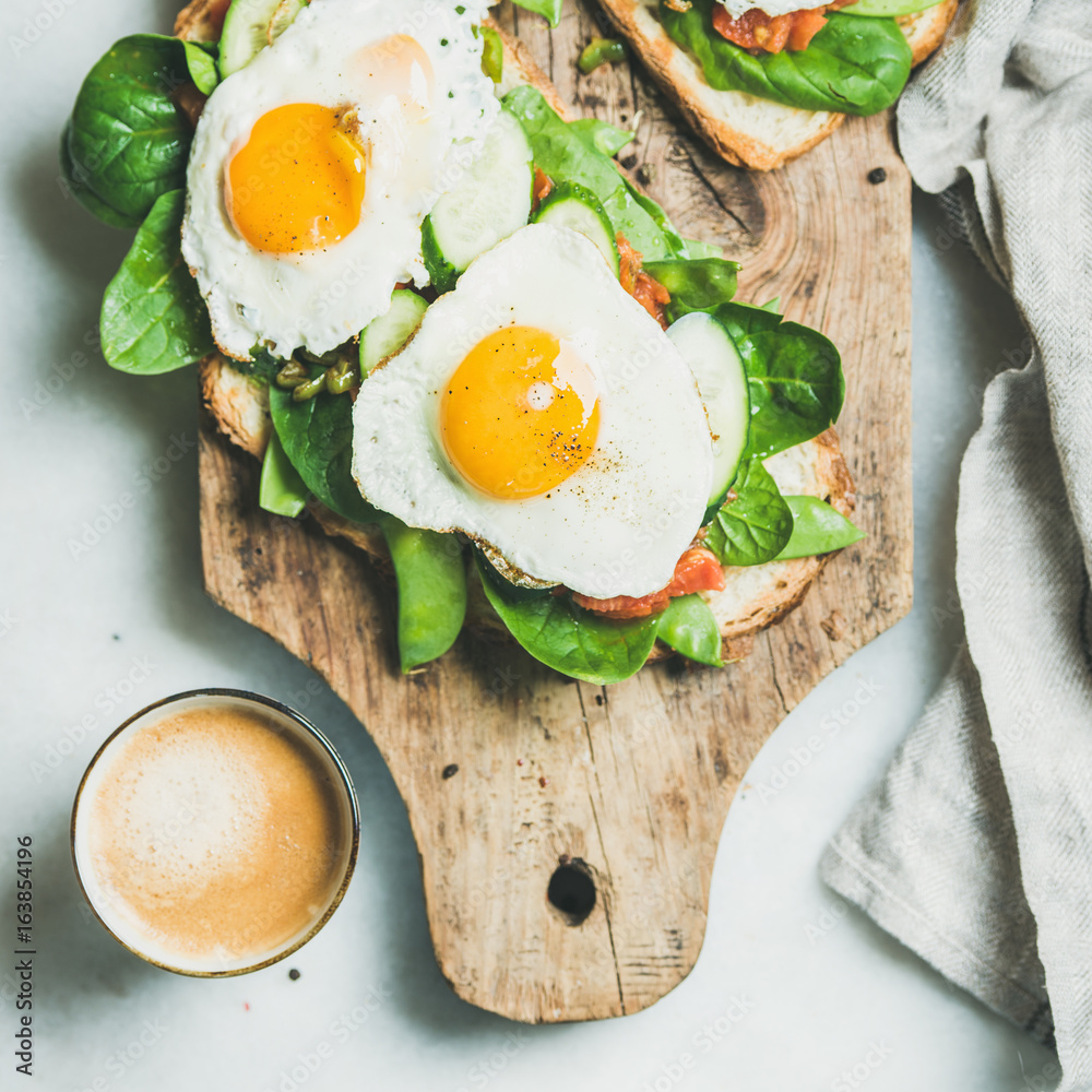 Healthy breakfast sandwiches and cup of coffee. Bread toasts with fried eggs and fresh vegetables on