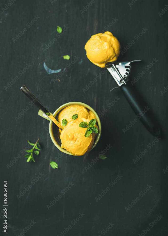 Refreshing summer dessert. Mango sorbet ice cream scoops with fresh mint in green cup over black woo