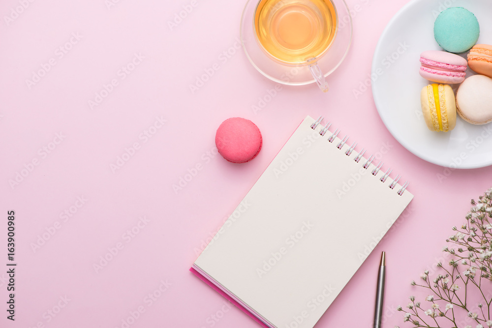 放在粉色桌子上的平板笔记本、蛋糕马卡龙、一杯茶和一朵花。美味的mac早餐