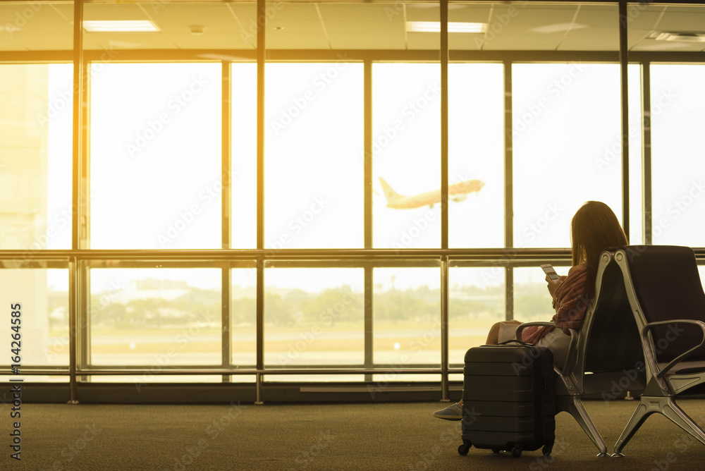 机场年轻美女拿着旅行袋在机场用智能手机等待航班，世界前任