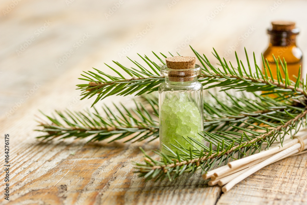 cosmetic spruce oil and salt in bottles with fur branches on wooden table background