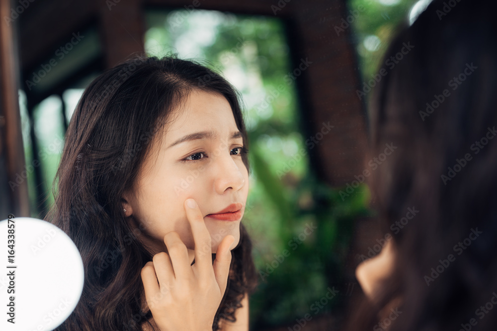 美丽，护肤生活方式理念。年轻的亚洲痤疮女性看着镜子。