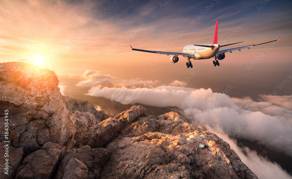Airplane is flying over clouds at sunset. Landscape with white passenger airplane, mountains, sea an