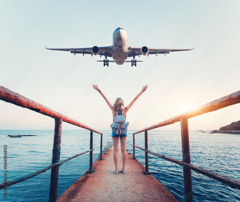 日落时的飞机和女人。夏天的风景，女孩举起手臂站在码头上