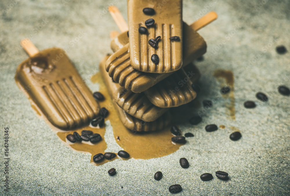 Summer healthy vegan frozen dessert. Flatlay of melting coffee latte popsicles with coffee beans ove