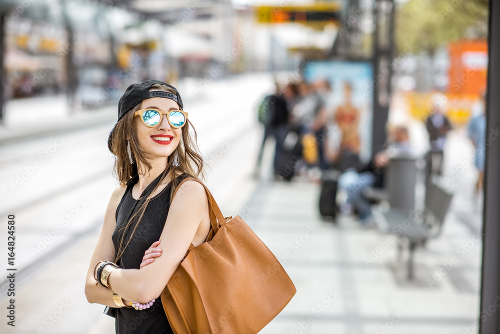 一位穿着黑色连衣裙、戴着帽子、拿着包站在t电车站上的时尚女性的生活方式画像