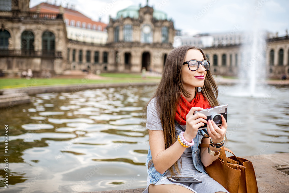 年轻快乐的女游客拿着相机坐在德累斯顿老城的喷泉上，