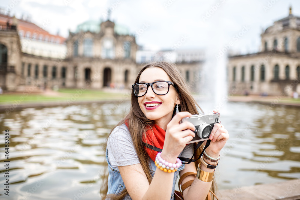 年轻快乐的女游客拿着相机坐在德累斯顿老城的喷泉上，
