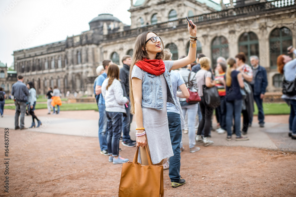 年轻微笑的女人在与旅游团参观旧宫殿i时用智能手机拍照