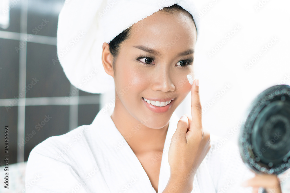 亚洲女性在浴室洗澡后，正在脸上涂面霜和乳液。