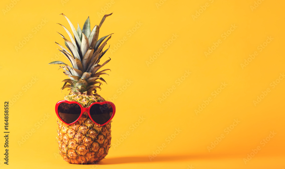 亮黄色背景上戴着太阳镜的整个菠萝