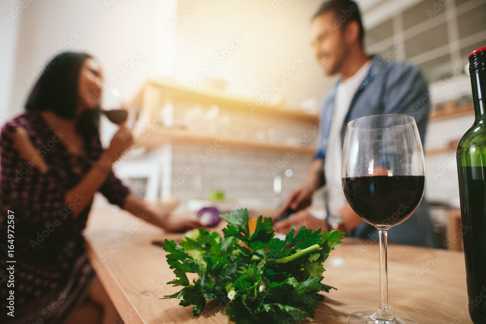 厨房柜台上的一杯红酒，背景是情侣