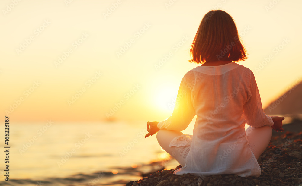 女子在日落海滩上练习瑜伽并以莲花姿势冥想
