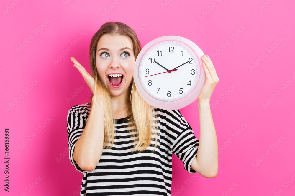 Young woman holding a clock on a pink background
