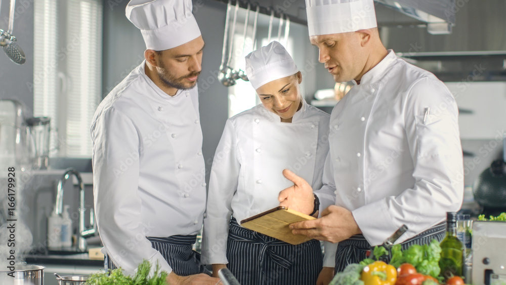 在现代厨房团队中，厨师们使用平板电脑制作食谱，他们微笑着进行讨论。