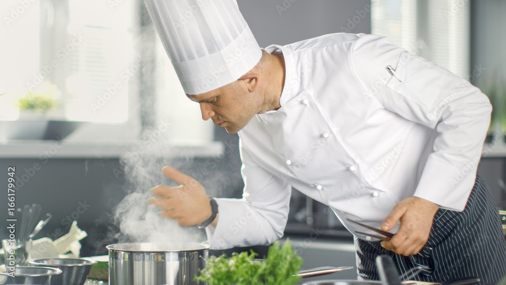 著名餐厅厨师从Saucepan闻到蒸汽味。他在现代厨房烹饪菜肴。