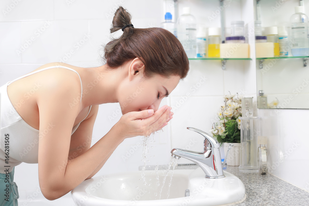 一名妇女在浴室水槽上方用水洗脸。