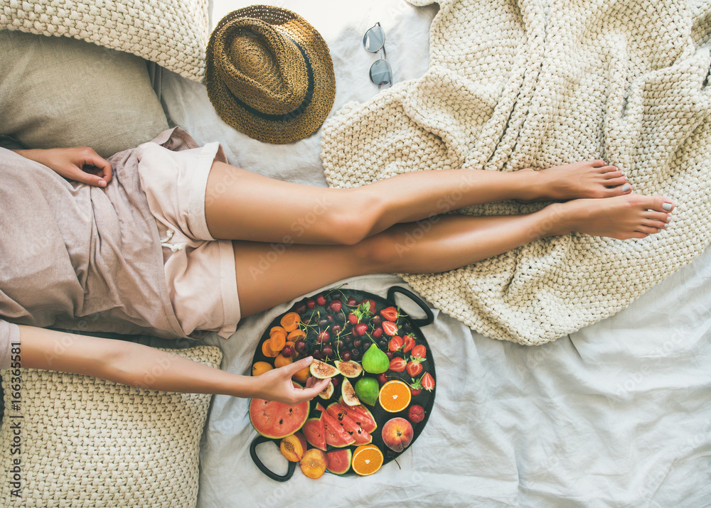 夏季健康生素食主义者在床上吃早餐的概念。年轻女孩穿着浅色的ho