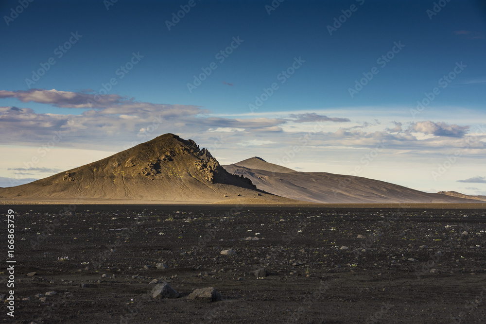 Brown isolated mountain with black volcanic ashes field and blue sky in summer, Landmannalaugar, Ice