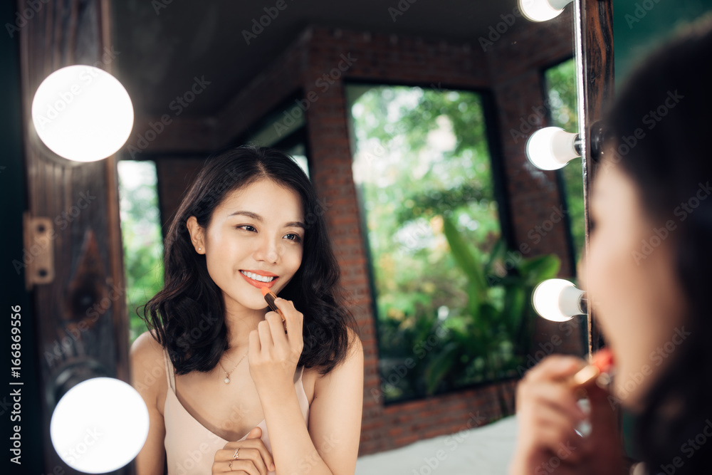 美丽的年轻女人在家化妆镜前涂上光滑的口红