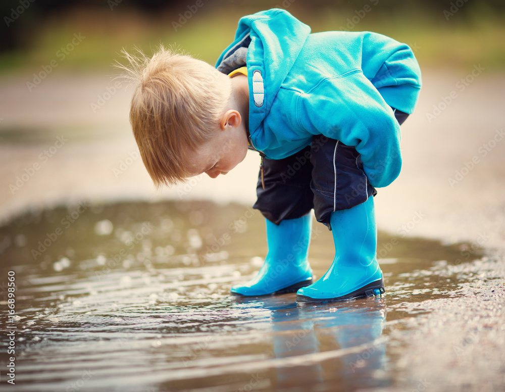 雨天孩子穿着雨鞋在水坑里行走
