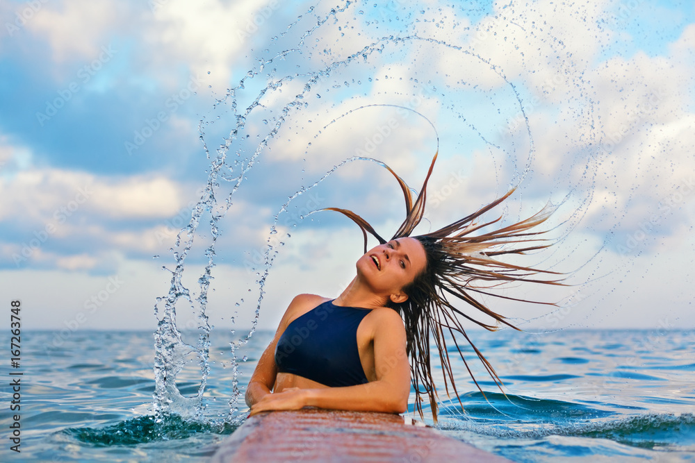 快乐的女孩在冲浪后玩得很开心。游泳冲浪者拿着冲浪板，用飞溅物翻转头发。水