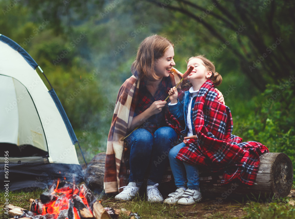 徒步旅行的快乐旅游家庭。母亲和孩子在帐篷附近的篝火上炸香肠。